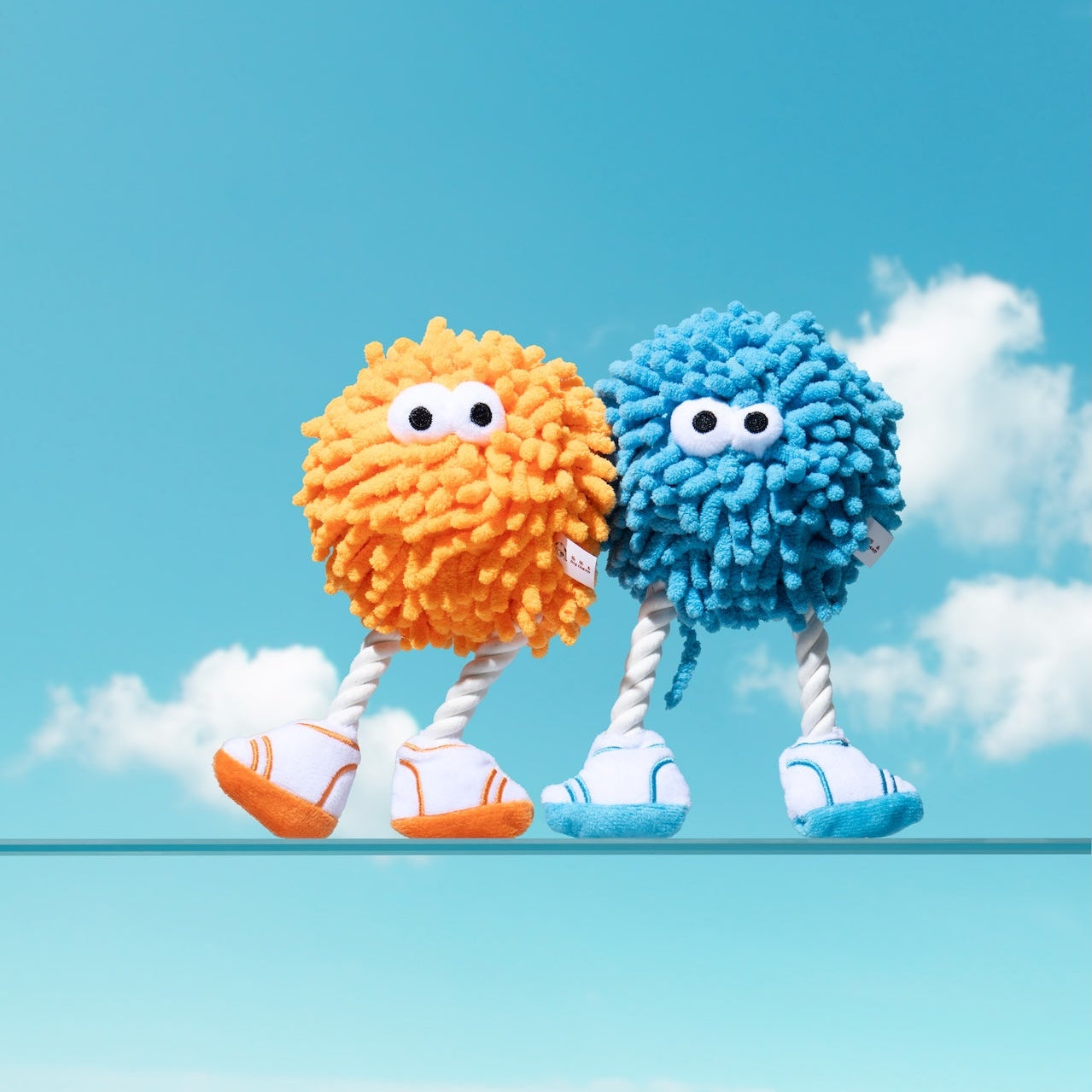 Two colorful, fluffy characters standing on a blue background with clouds.
